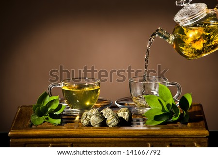 horizontal photo, of the glass teapot flow green tea in cup on brown background,  tea ceremony