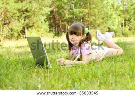 The small nice girl works on a computer, lays on a beautiful green lawn, pleasure