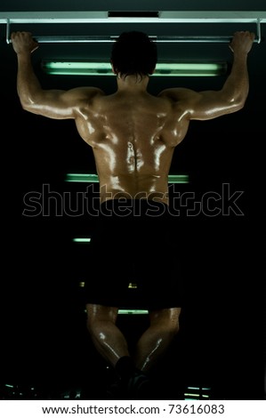 very power athletic guy ,  execute exercise tightening  on horizontal bar, in  sport-hall, glamour light