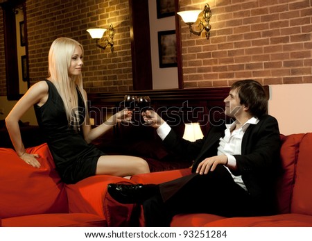 romantic evening date in hotel room,  happy couple with wine glass sit on red sofa