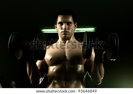 very power athletic guy ,  execute exercise with  dumbbells, in  sport-hall
