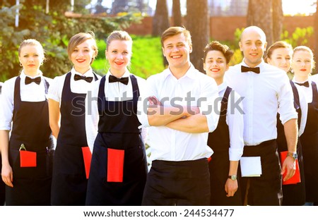 Large group of waiters and waitresses standing in row.