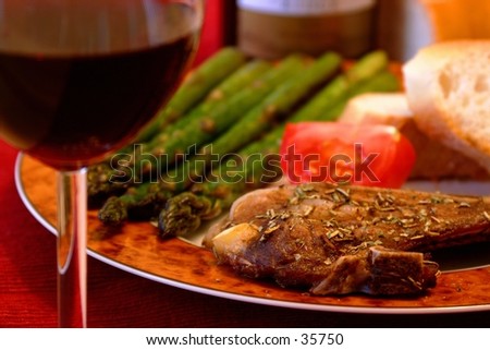 Meal of porkchops, asparagus, tomatoes and bread. Glass of wine in the foreground with shallow DOF.