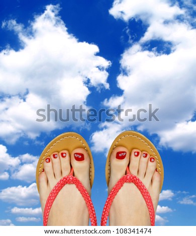 woman pedicured feet in flip flops on blue sky background