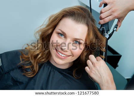 attractive woman in  hairsalon making new hairstyle with hair curler
