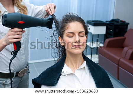 stylist drying attractive woman hair in salon