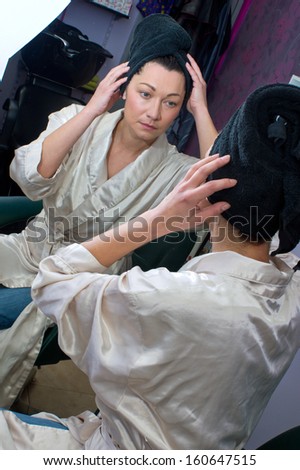 attractive mature woman in hair salon with towel on her head looking in the mirror