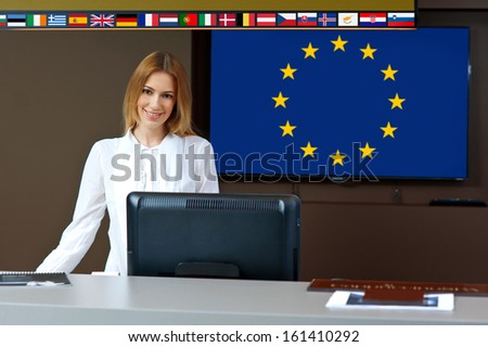 attractive woman at reception desk with european union flags behind her