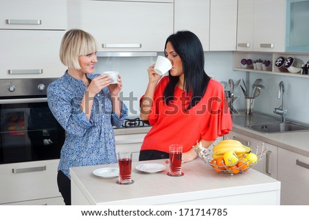 two attractive woman friends drinking coffee and chatting in kitchen