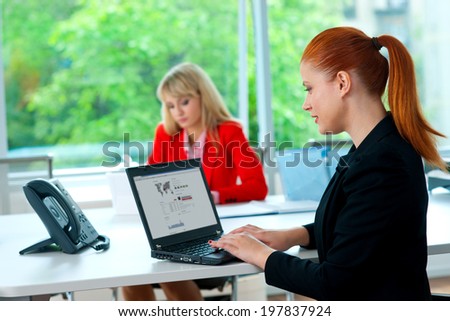 attractive red hair business woman in office with tablet computer and colleague in the background