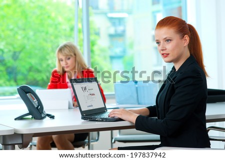 attractive red hair business woman in office with tablet computer and colleague in the background