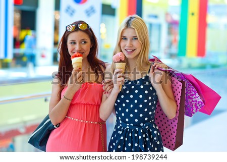 two attractive girls with ice cream and shopping bags walking