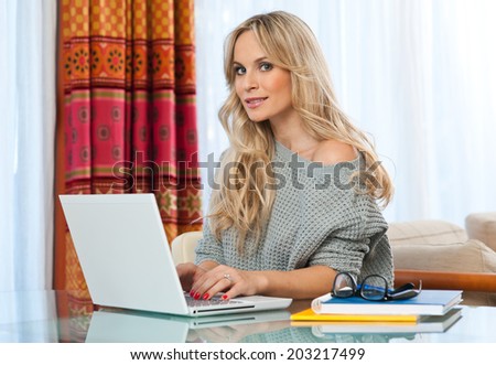 attractive blond woman writer sitting at the table and writing on the laptop computer