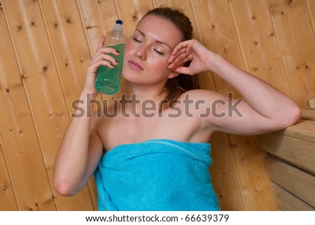 woman sweating in sauna and cooling herself with cold energy drink bottle