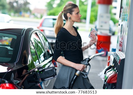 woman holding gas nozzle and money in gas station