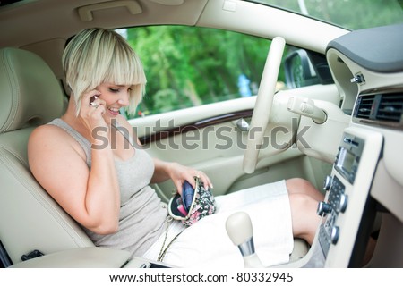 woman sitting in drivers seat of her luxury car talking to mobile phone and searching purse