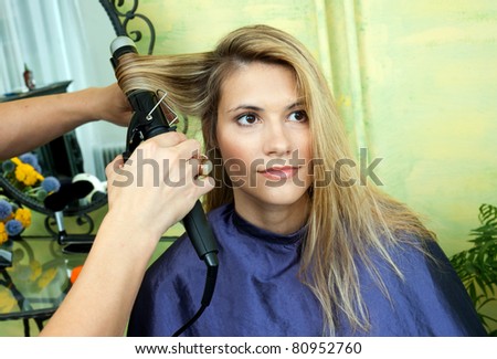 stylist curling woman hair in salon