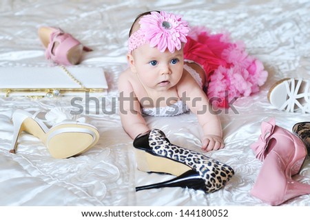 baby girl wearing tutu laying on the bed with high heels shoes and bags