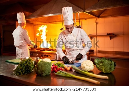 А team of professional chefs cook meals with frying pan and fire in the kitchen of restaurant.  Chief chef preparing dish using different food ingredients, vegetables, meat and fish Сток-фото © 
