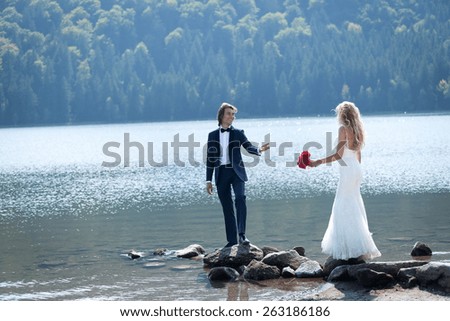 Married couple having a relaxing and fun moment at the lake. The groom dares his bride to follow his steps on some rocks.