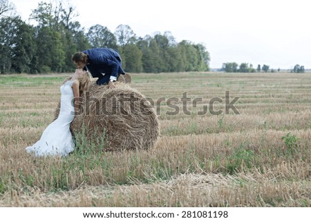 Beautiful married couple acting very romantic on a field of bales. He climbs the bale to kiss her lips while she lays her head to be kissed.