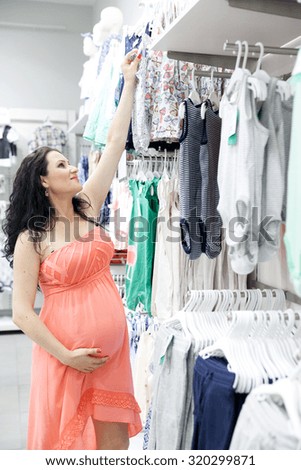 Lovely young pregnant woman looking for some baby clothes in a store for her new baby.