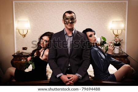 A man with a mask and two ladies with roses. See more images from the same shoot.