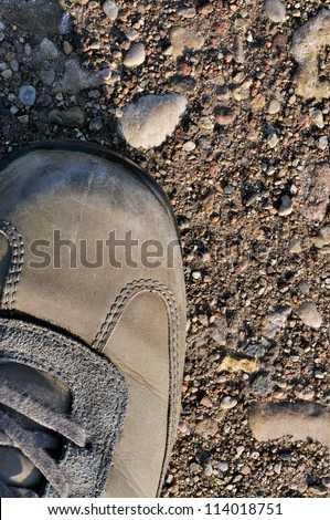 Hiking boot off-road shoe on hard arid dried soil, rough terrain vertical close up, detailed macro of bare earth, dust, stones, rocks, pebbles, sand, ash