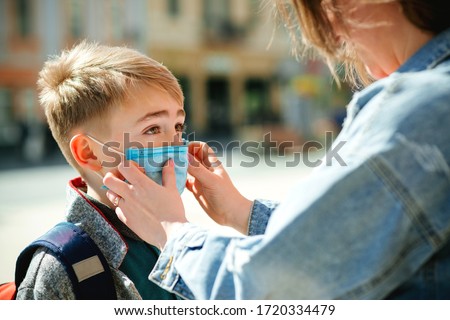 Mother puts a safety mask on her son's face. Schoolboy is ready go to school. Cute boy with a backpack outdoors. Back to school concept. Medical mask to prevent coronavirus. Coronavirus quarantine