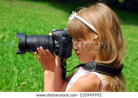 beautiful young girl taking photos by professional reflex camera on green meadow