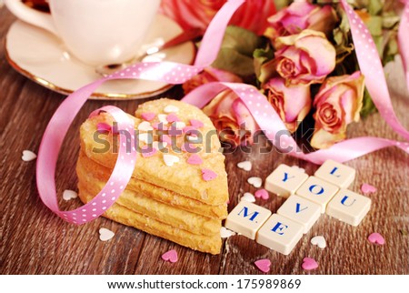 love words made of scrabble letters ,dried roses  and heart shaped cookies with sprinkles  for valentine on wooden table