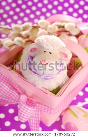 pink easter basket with eggs and funny sheep figurine on purple dotted background