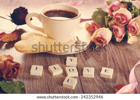 I love you made of letter cubes ,dried roses ,cup of coffee and heart shaped cookies with sugar for valentine on wooden table in vintage style