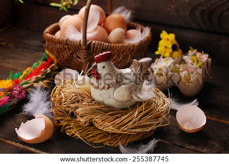 easter decoration of hen figurine in the nest and wicker basket with eggs on wooden background