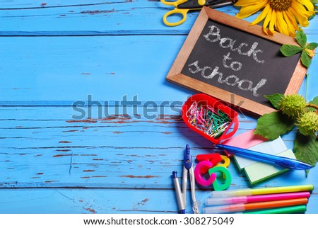 school equipment border with text  Back to school written by chalk on small blackboard  on blue wooden background