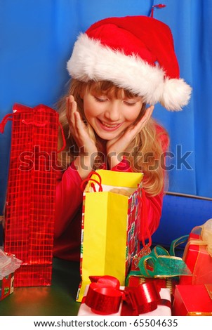 young girl in santa`s hat surprised with christmas gifts on blue background