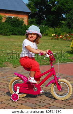 little girl learning to ride a bicycle with training wheels