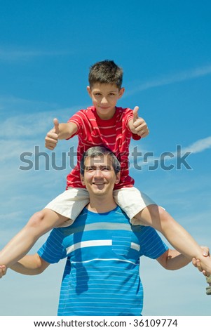 a child in a red shirt is sitting on his father in a blue shirt outdoor