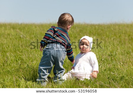 A little boy helps a toddler girl to get up in the meadow