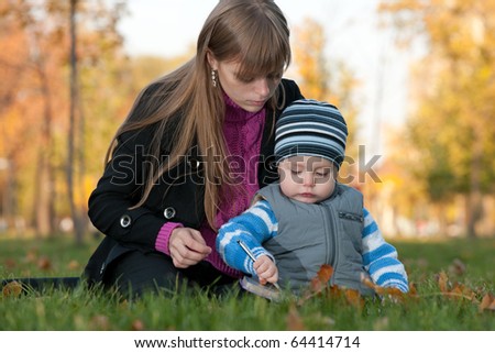 A mother is teaching her little son to draw while walking in the autumn park