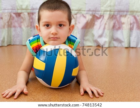 A little smiling boy is lying on the floor holding his head on the ball