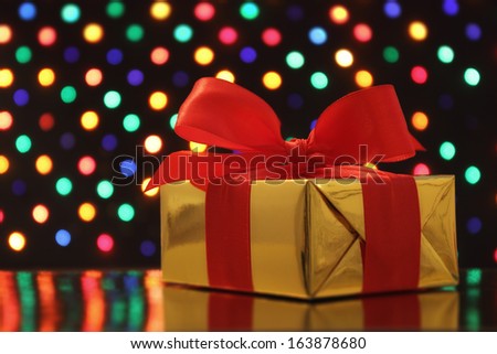Gift wrapped present with a bow in front of a festive garland lights soft-focus background