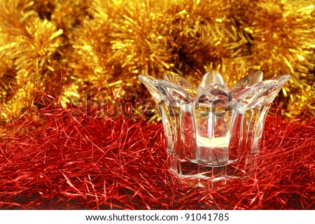 Lit candle in a transparent glass candlestick on a festive red and gold glitter background