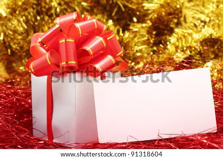 Silver gift wrapped present with red bow and blank greeting card on a festive red and gold glitter background