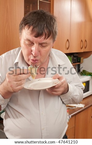 The elderly thick man tasty eats something on kitchen.Manti (dumpling).