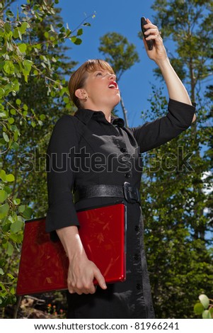 Frustrated business woman in the forest searching for a cell phone signal.