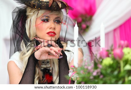 beautiful bride wearing black net gloves and unusual hat sits at table and looks at candles