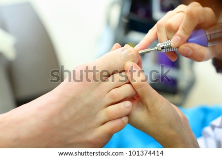Female hands polish male toes by special machine in beauty salon
