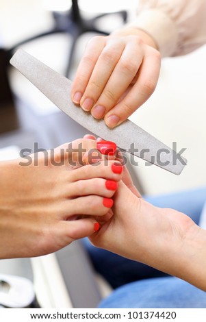 Female hands make pedicure by nail files for client in beauty salon