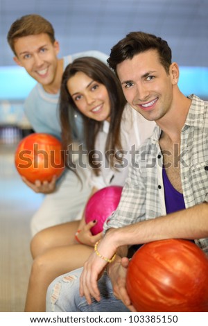 Two beautiful men and woman hold balls in bowling club; shallow depth of field; focus on right man